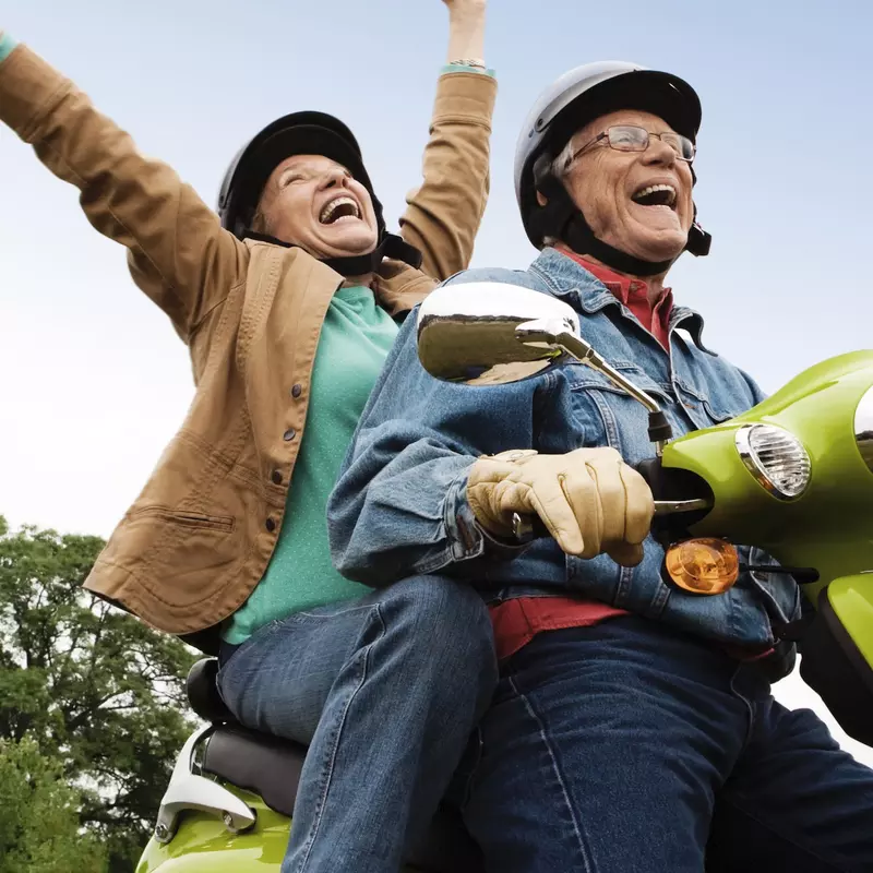 A joyful couple takes a ride on a scooter.