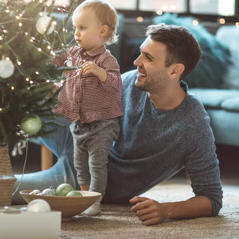 A father and his toddler trim a Christmas tree.
