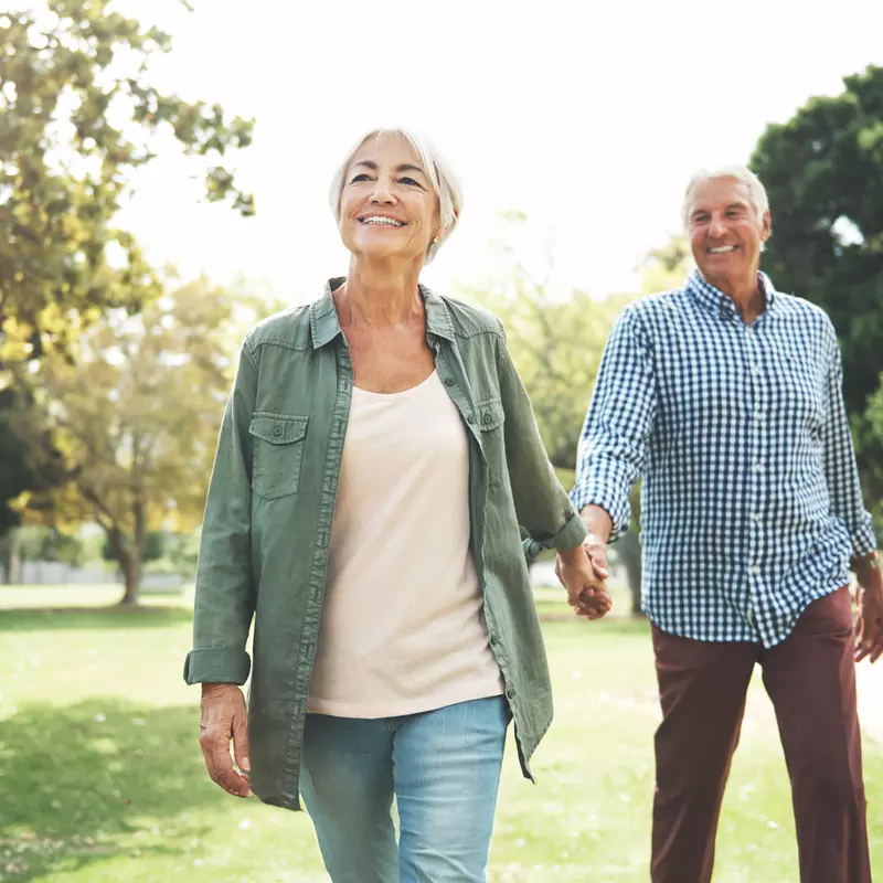 Elderly couple holding hands and walking in a park