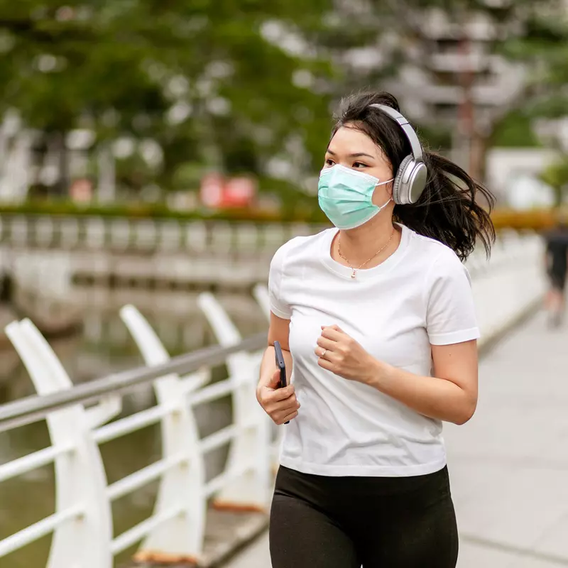 Woman running in a park outside while wearing a mask.