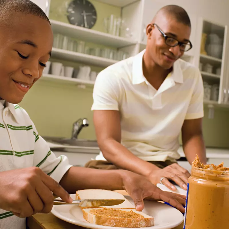 Father and son make peanut butter sandwiches together.