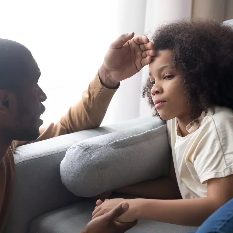A black man checks his daughter for a fever