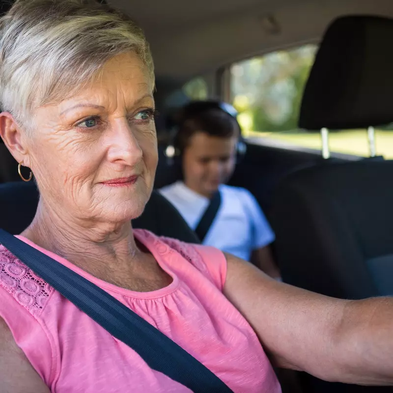 A grandmother driving with her grandson in the back seat.
