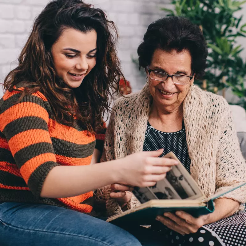 A grandmother and granddaughter look at a photo album together.