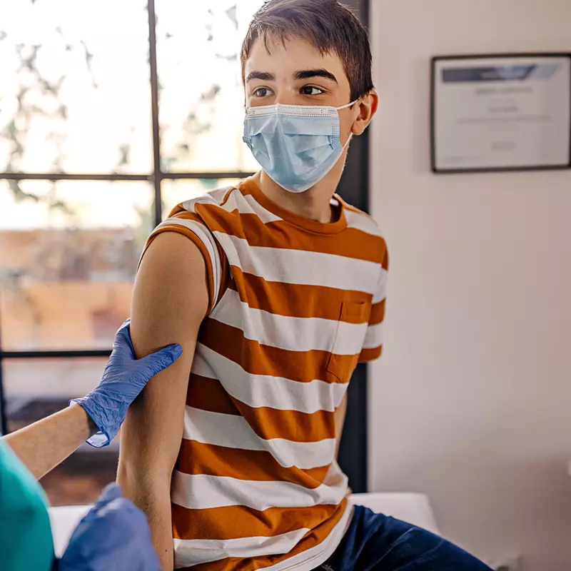 A teenager getting a vaccine shot by a nurse