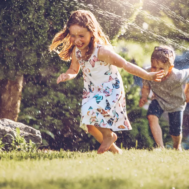 Two children playing in the yard with sprinklers.