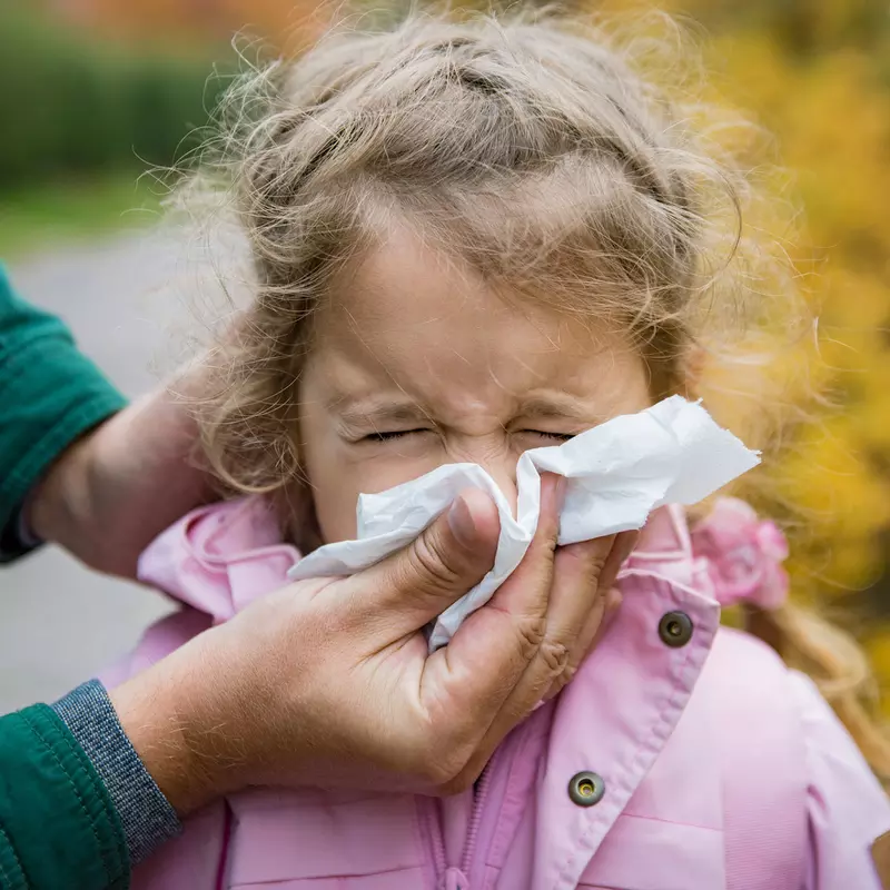 With the help of her mom, a little girl blows her nose