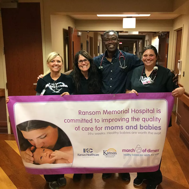 Physician and nurses holding a banner of the work they do for mothers and babies.