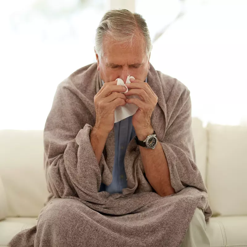 A man sneezing while at home on his couch. 