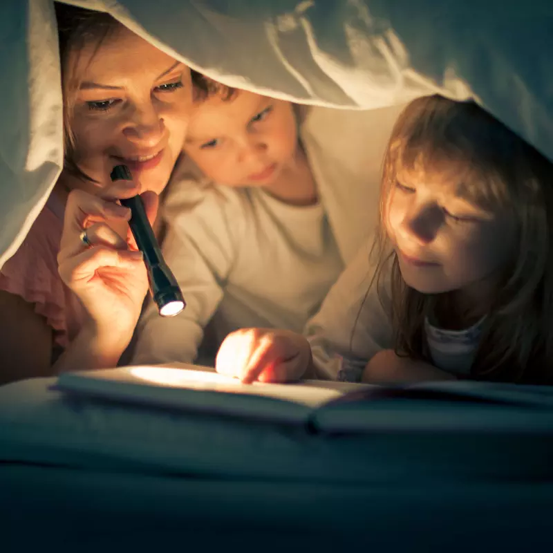 A mother, daughter, and son reading bedtime stories underneath the sheets