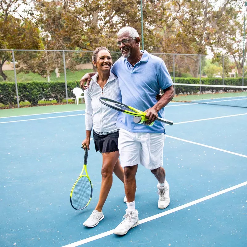A mature couple laughs together after a lively game of outdoor tennis