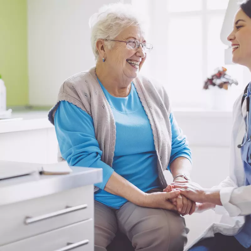 An older woman laughs with her doctor during a visit.