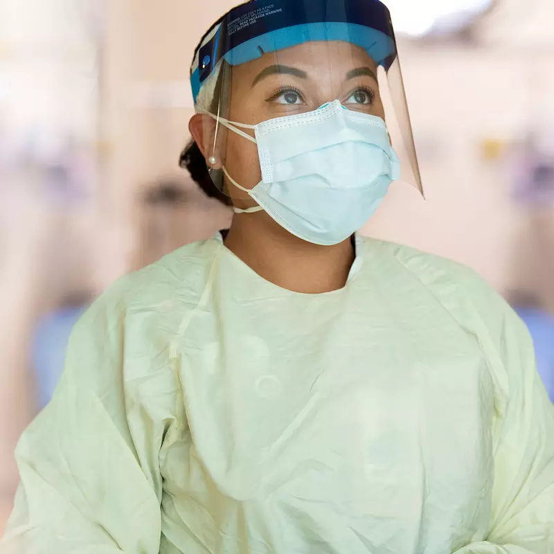 A nurse, dressed in proper personal protection equipment, stands praying.