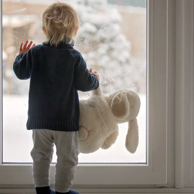 A toddler looks at the snow through a window.