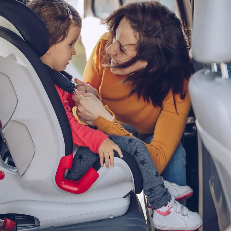 A mom buckles her toddler into her carseat.
