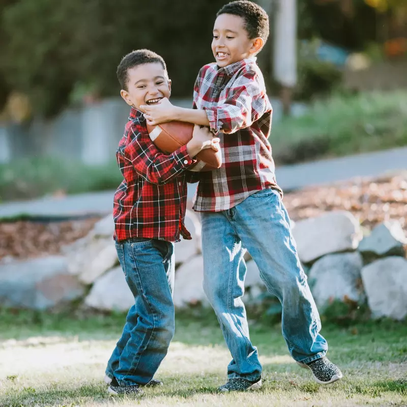 Two young boys playing football outside.