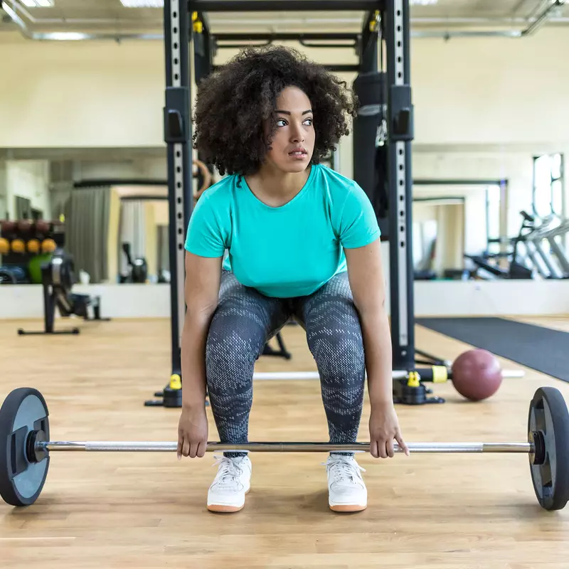 A young black woman lifts a barbell at the gym