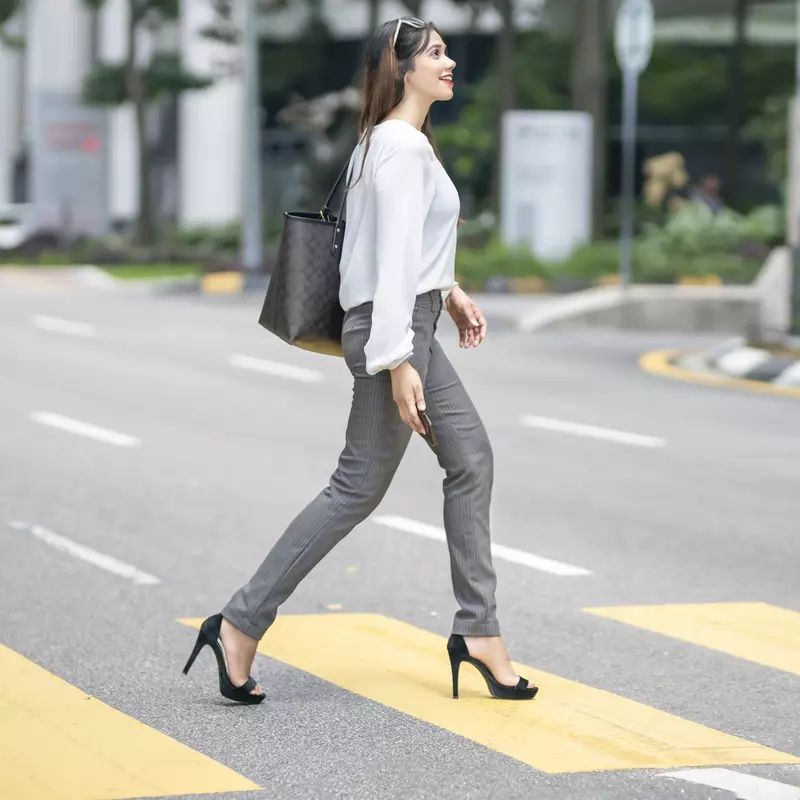 A woman crosses the street wearing high heels.