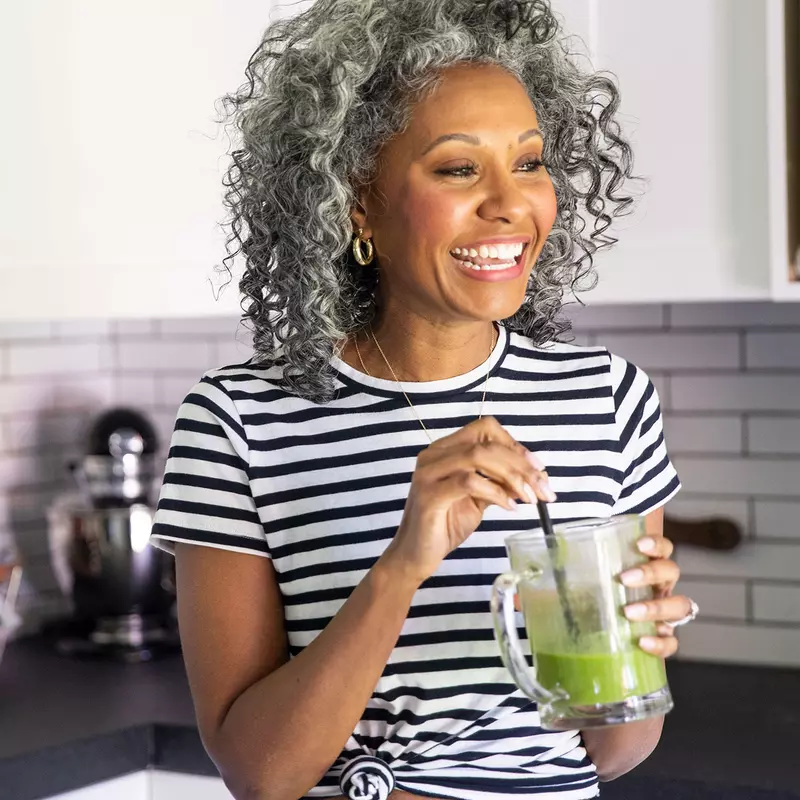 A woman drinking a healthy green smoothie in her kitchen.