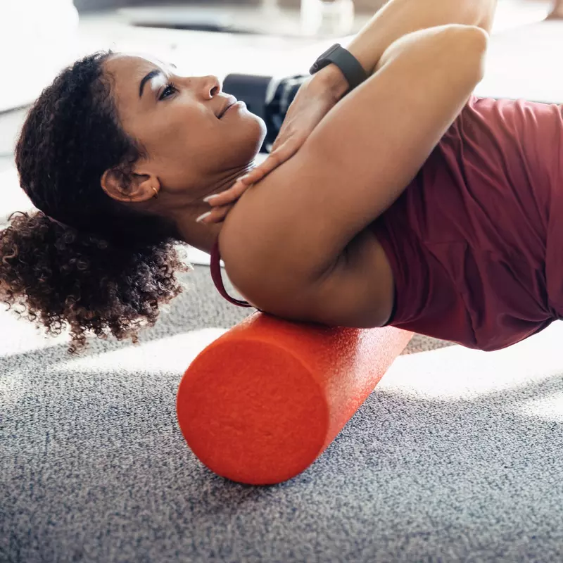 A woman foam rolling her upper back.