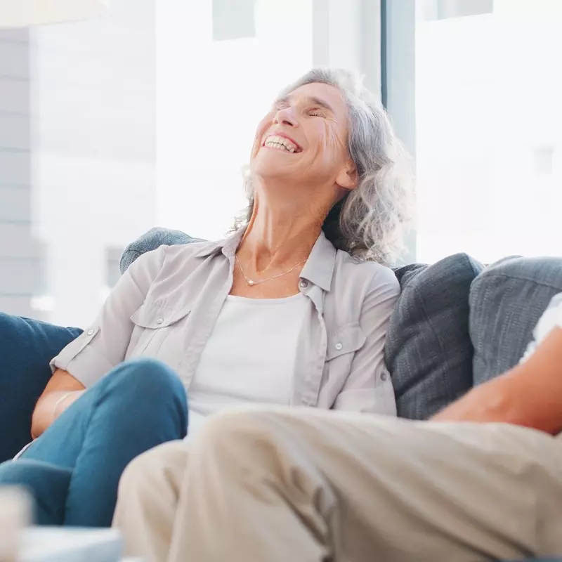 A woman laughing while sitting on the couch with her spouse.