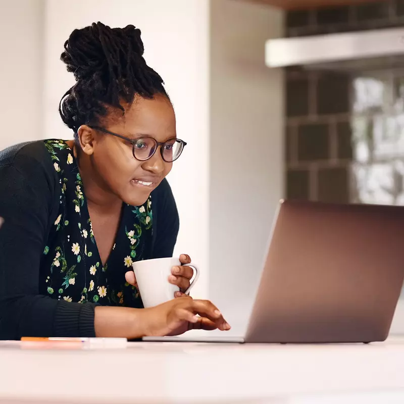 A black woman researches on her laptop while drinking coffee