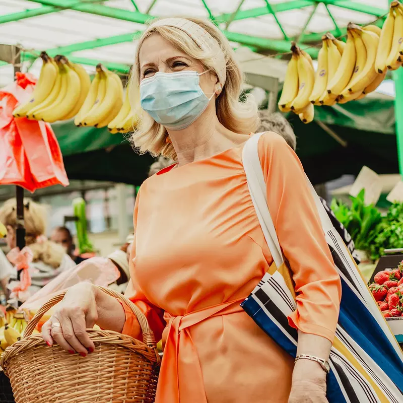 A woman wearing a mask at an outdoor farmers market.