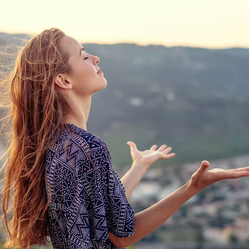 A young woman gives praise to God outside