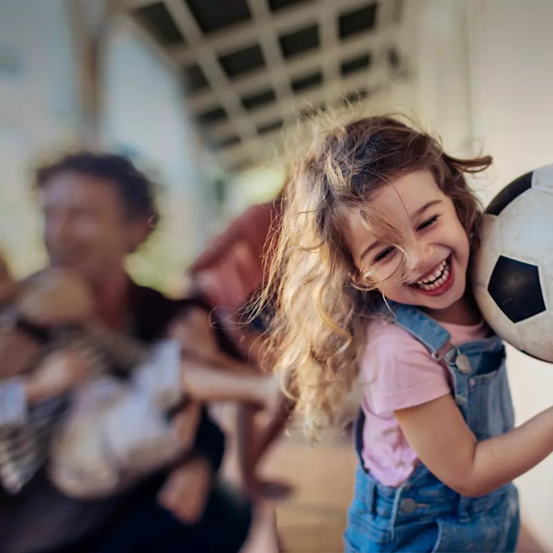 Young girl running with her family and carrying a soccer ball