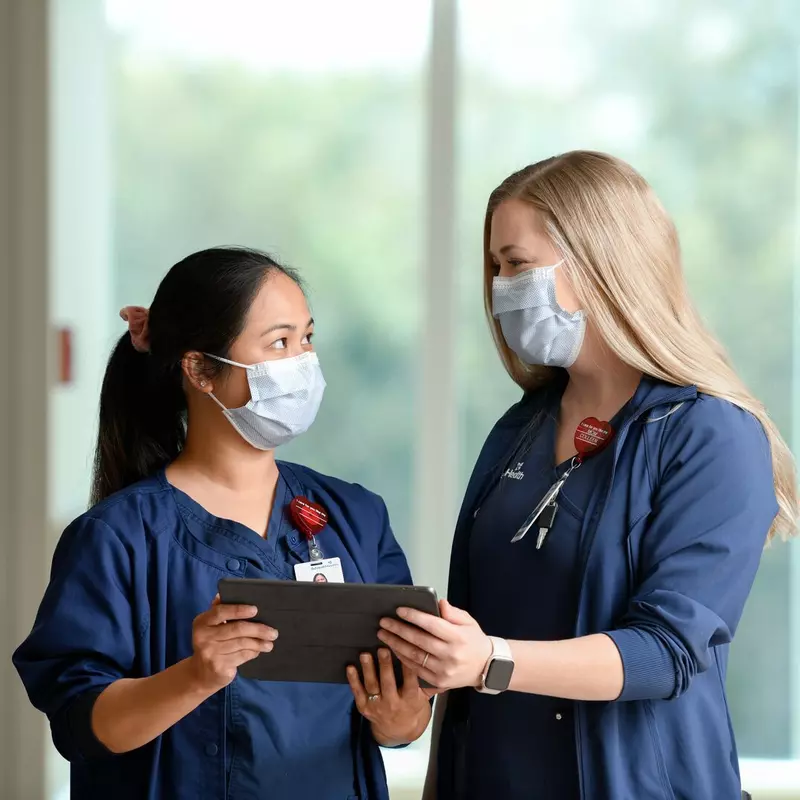Two nurses looking at each other, holding a tablet