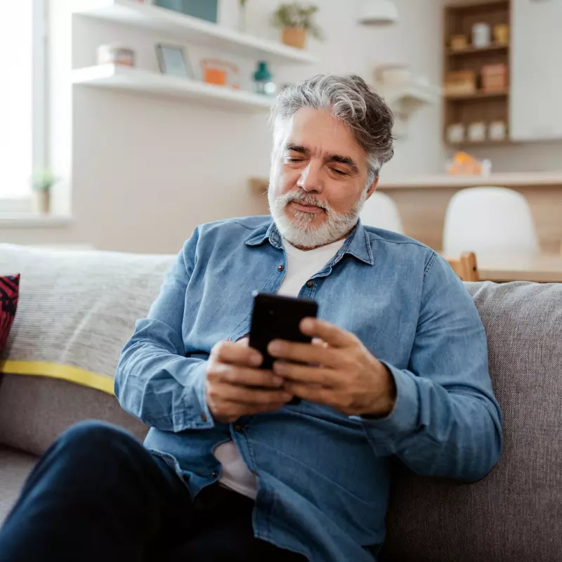 Older man looking at his phone while sitting on a couch.