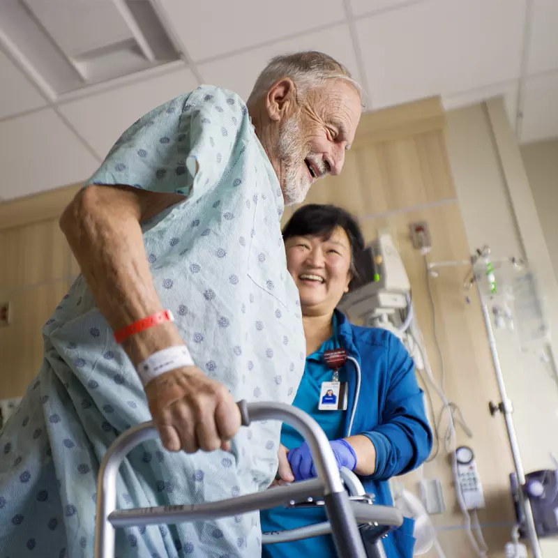 Older man using a walker with the help of a nurse
