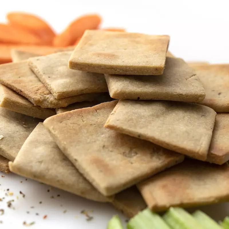 Pile of square crackers next to celery and carrot sticks