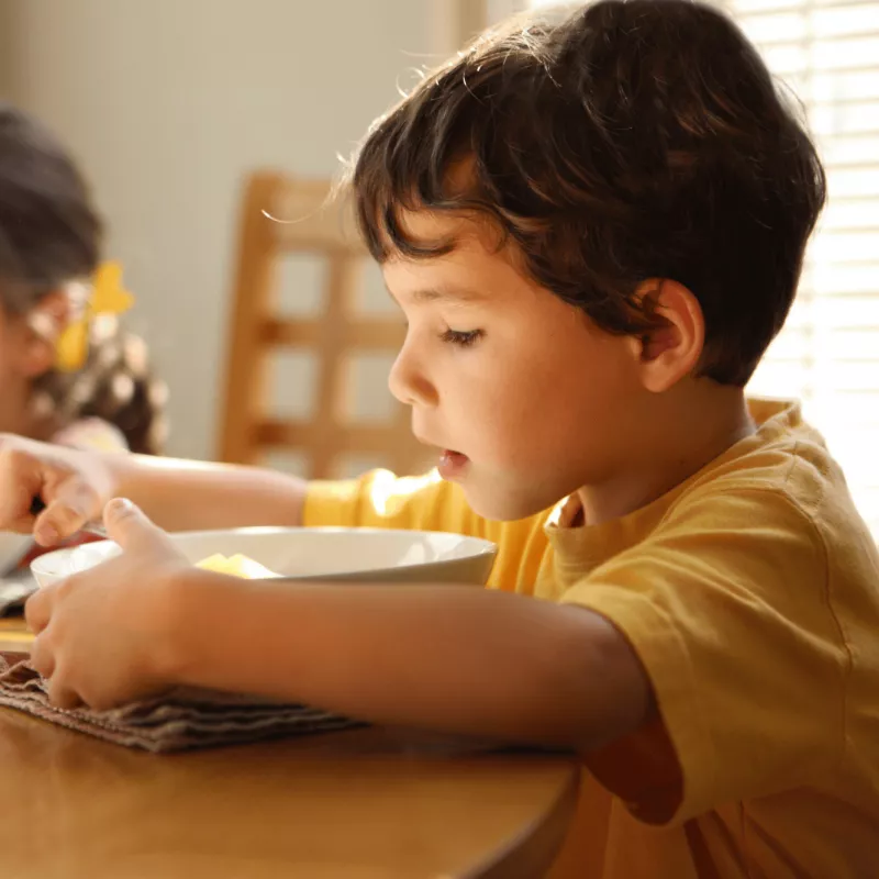 A young boy and girl eating together while at a dining room table together.