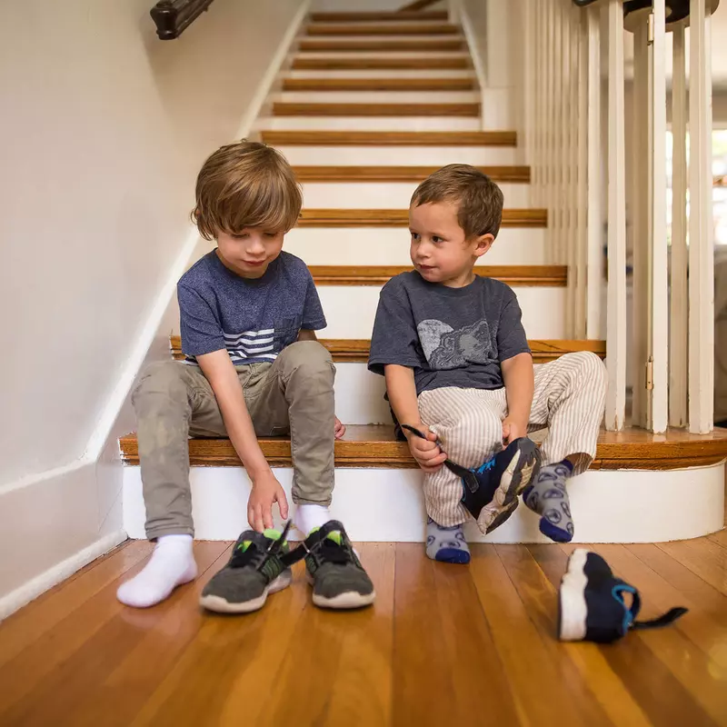 Two brothers getting ready to go out while putting their shoes on.