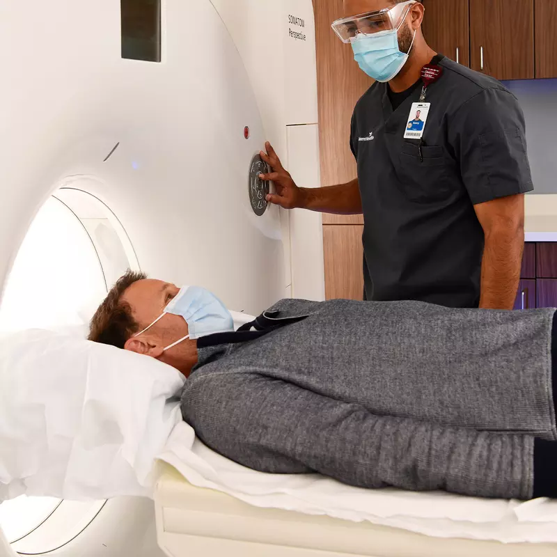 Man getting a CT scan while him and imaging tech wear masks.