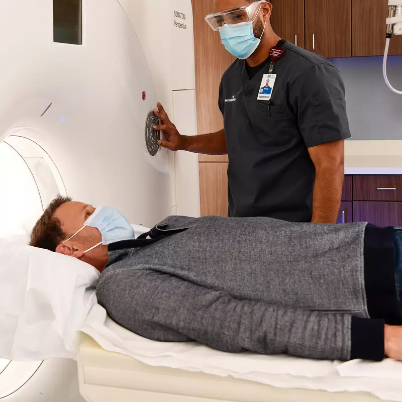 Man getting a CT scan while him and imaging tech wear masks.