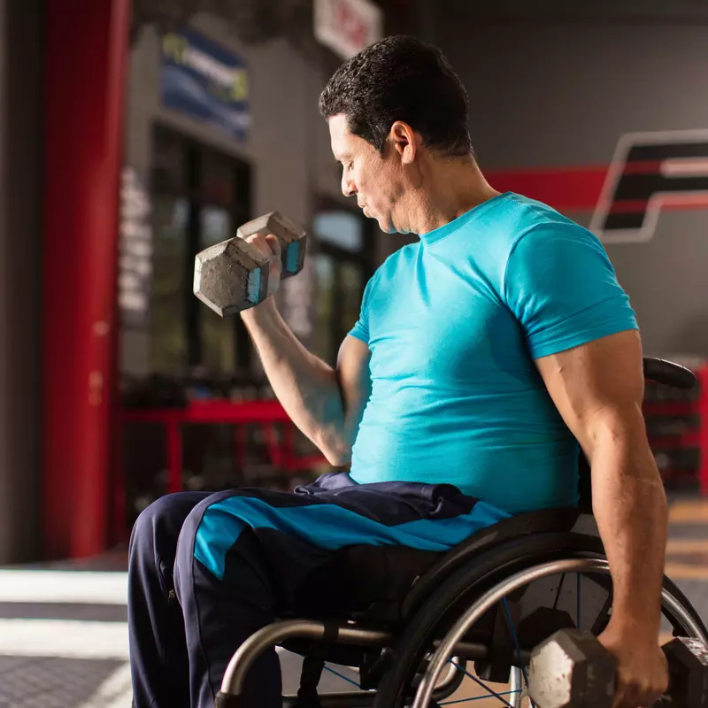 Man in a wheelchair lifting a dumbbell weight with his right hand. 