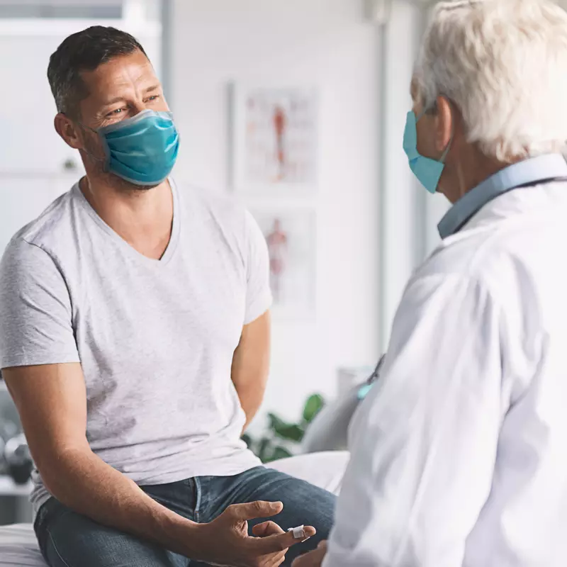 Man talking with doctor while both are wearing masks.