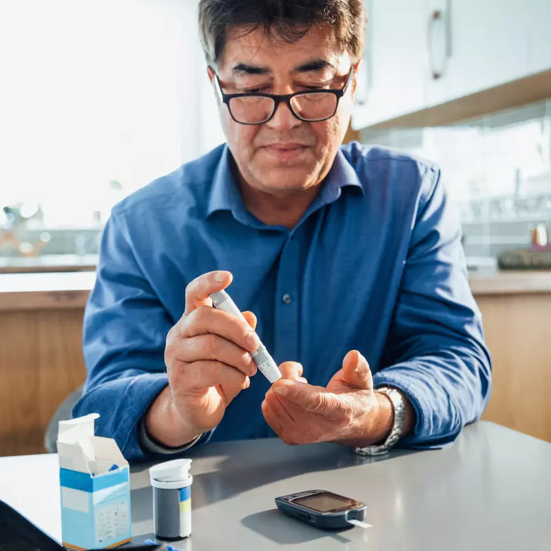 A man sitting in a kitchen using a glucose monitor.