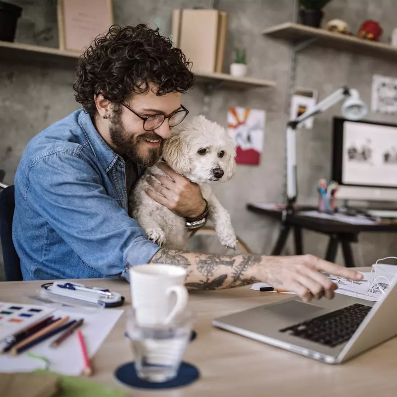 A man working on his laptop with his dog in his lap. 