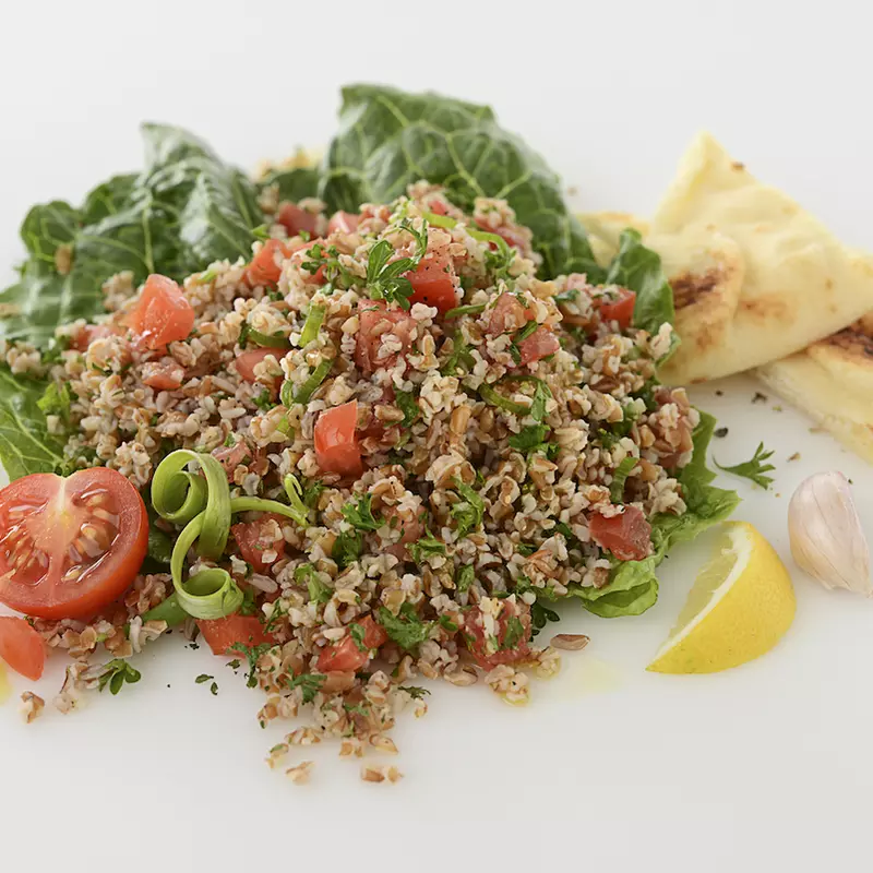 Mound of tabbouleh salad with pita, lettuce, tomato, and lemon garnishes