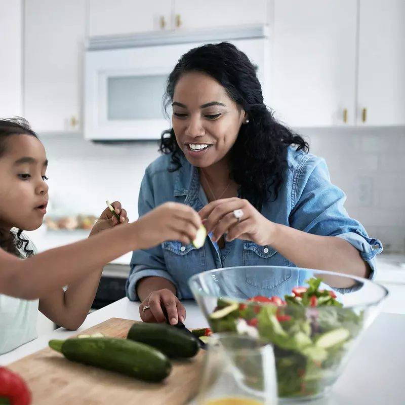 A mother and daughter prepare a salad at home. 