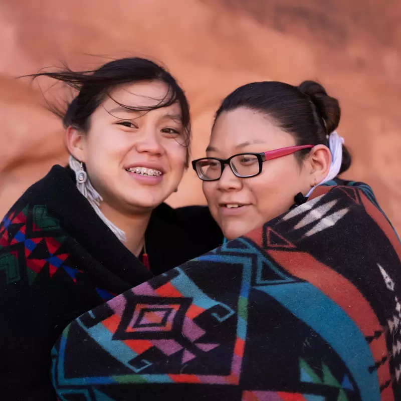 Native American mother and daughter wrapped in a blanket together while outdoors.