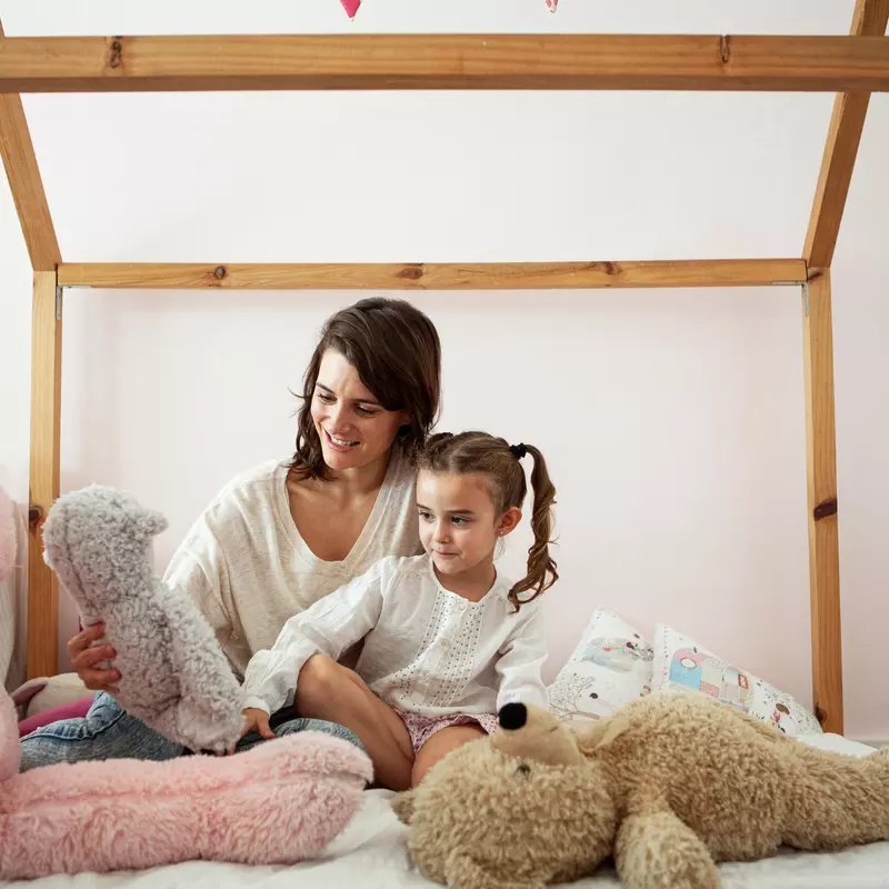 Mother and daughter on a bed with stuffed animals.