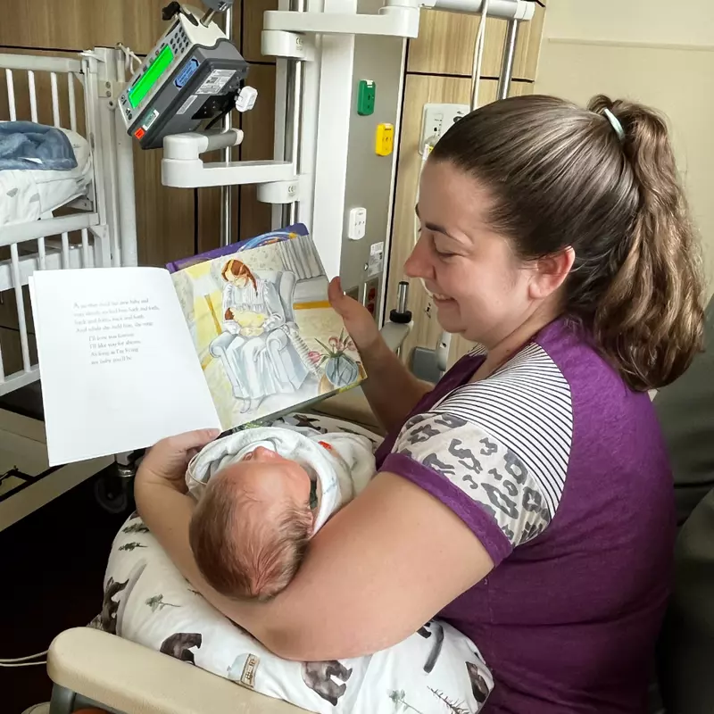 A mom reads to her baby in the AdventHealth for Children NICU in Orlando. Sitting in a rocking chair, she holds her baby while reading the book "Love You Forever."