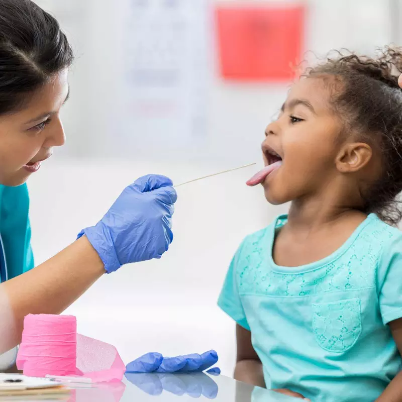A female nurse examines the tonsils of a young girl at a doctor appointment.