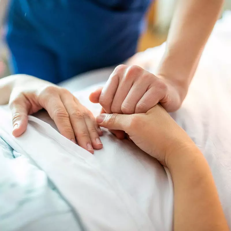 A nurse holding a patient's hand to comfort.
