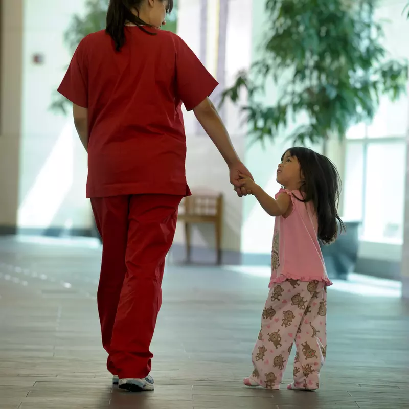A nurse walks a child patient to her room.