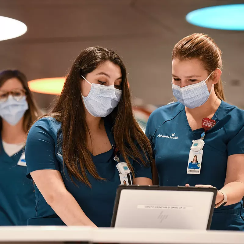 Two nurses looking at a laptop and talking while both wear masks.